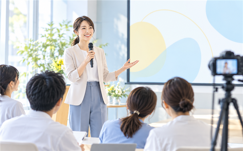 配信カメラを備えた会場で講演する女性